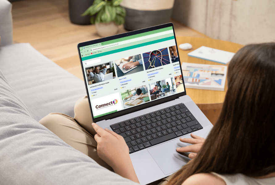 Woman sat on a sofa, with a laptop on her knees, selecting an online training course.